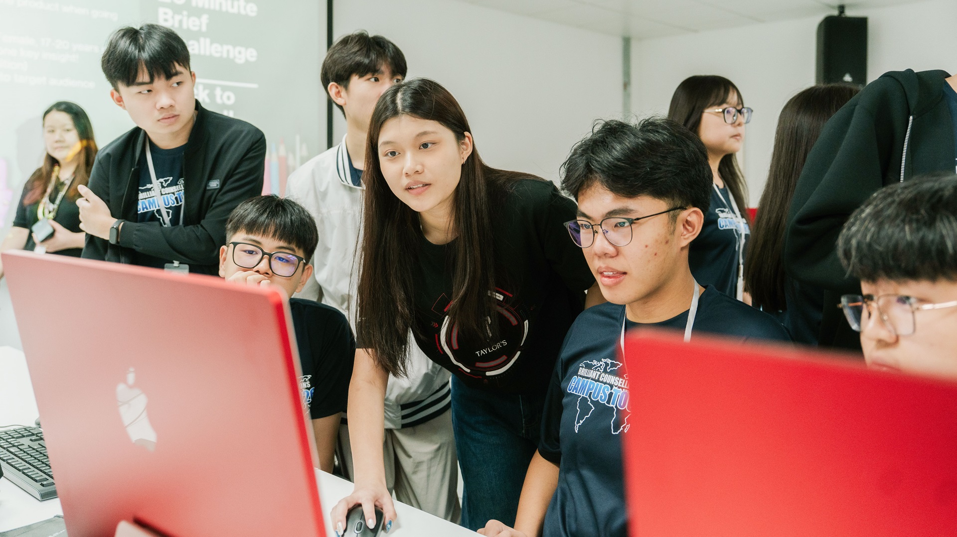 Taylor's diploma students gathering around a computer, with one student using the mouse while others focus on the task at hand.