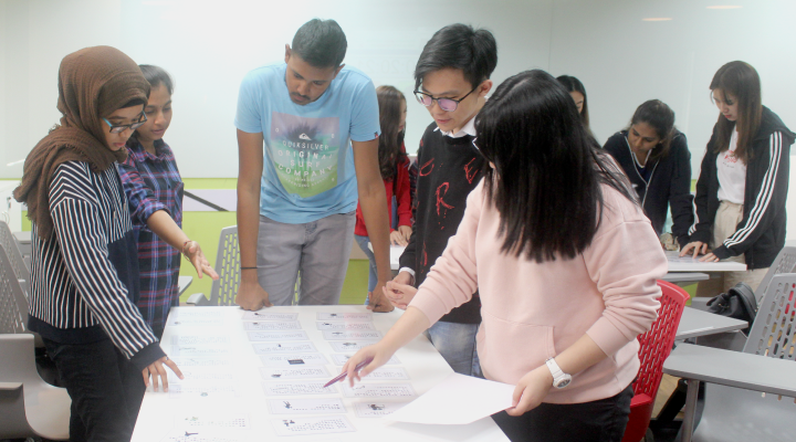 Five students discussing ideas by drawing on a paper
