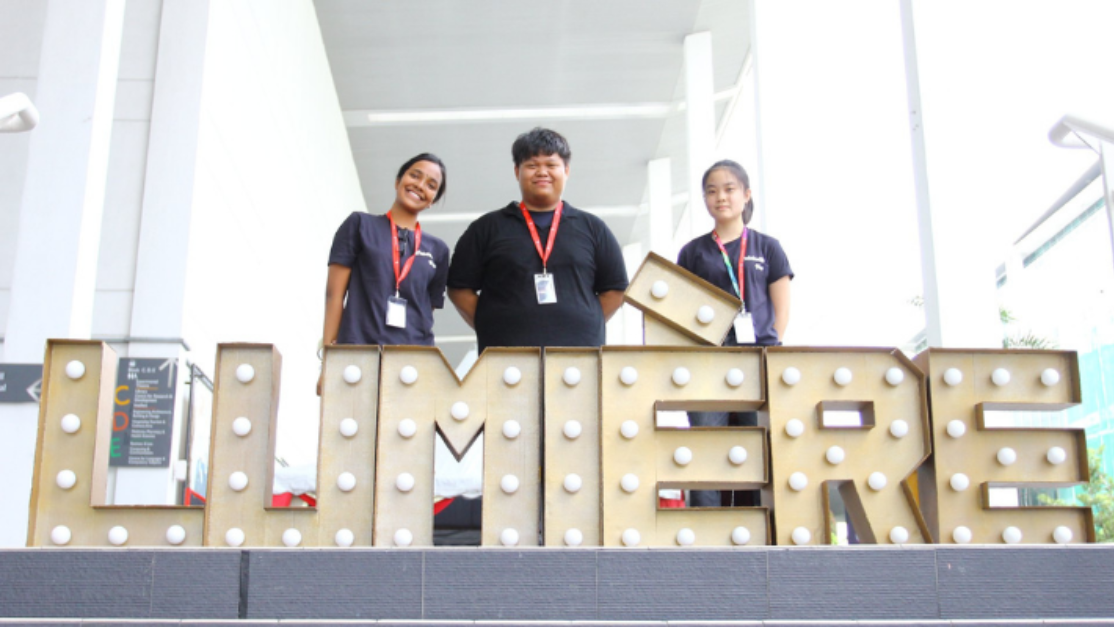 3 students in front of the lumiere word stand